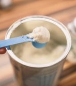 Powder milk for baby and blue spoon on light background close-up. Milk powder for baby in measuring spoon on can. Powdered milk with spoon for baby. Baby Milk Formula and Baby Bottles. Baby milk formula on kitchen background