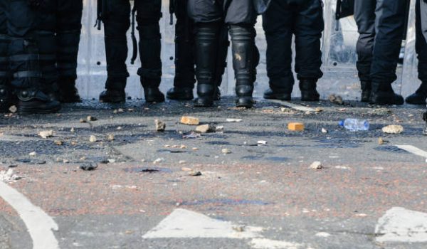 Stones and bricks litter the road as police riot squad move forward